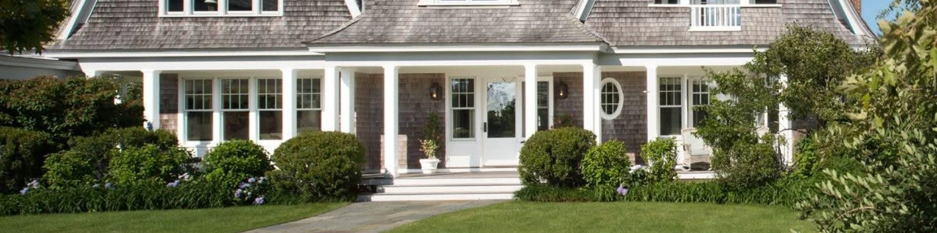 Shingled home with white trim, covered porch, and landscaped front yard