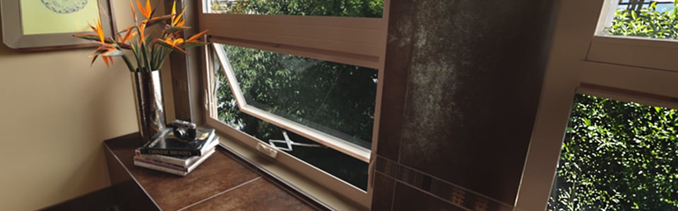 Awning window cranked open above a tiled sill holding a vase of flowers