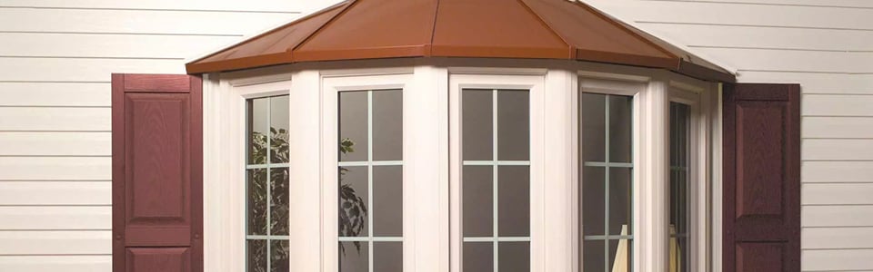 Bay window with a copper roof and grid panes projecting from white siding