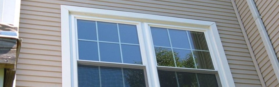 White double-hung windows with colonial grids set in tan lap siding