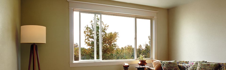 Horizontal slider window above a living room sofa, open to a treeline