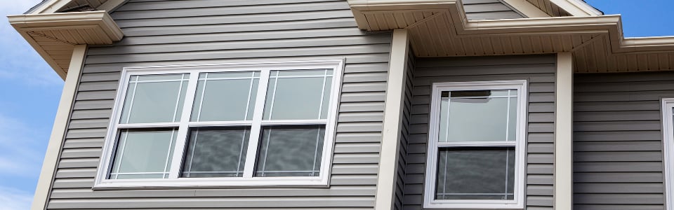 White double-hung windows with colonial grids set in tan lap siding