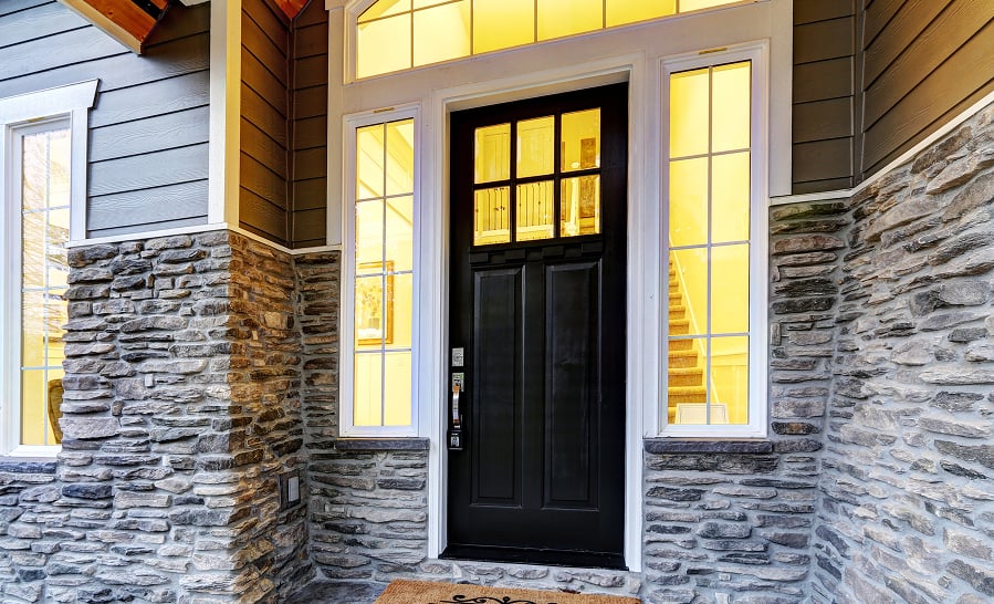 Black craftsman entry door with sidelights and a transom in a stone-and-shingle entry