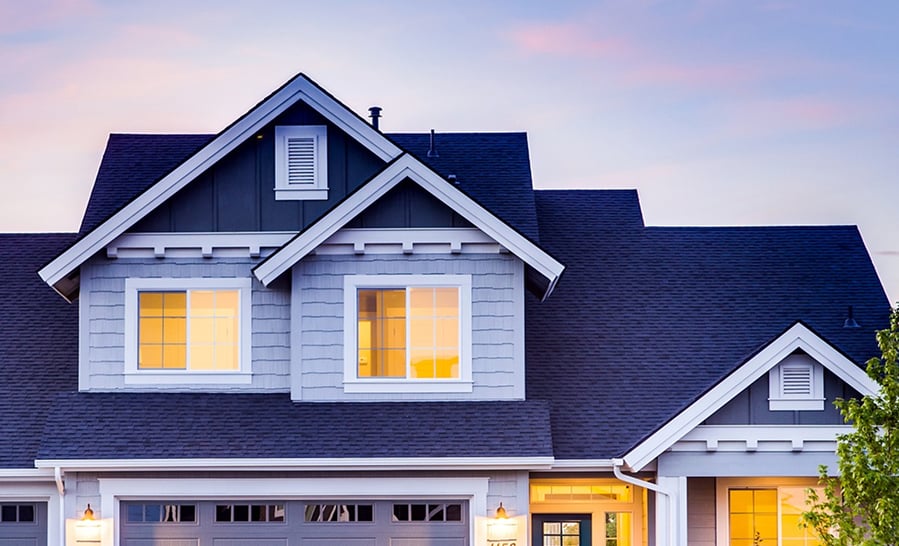 Gabled roofline of a two-story home at dusk with the windows lit from inside