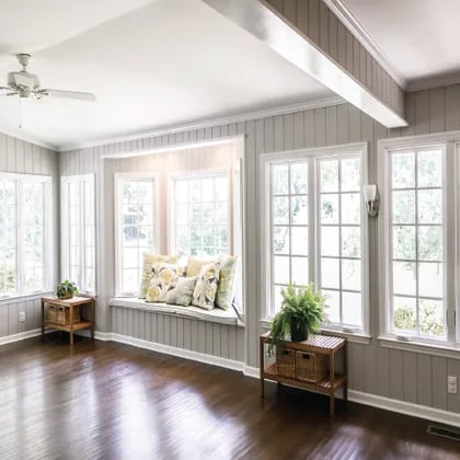 Sunroom with a cushioned window seat, wide white-framed windows, and dark hardwood floors