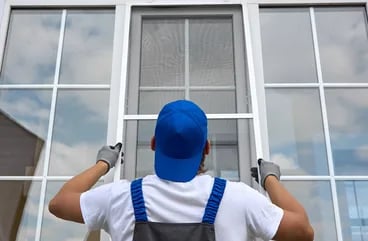 Installer in a blue cap fitting a new white-framed window from outside