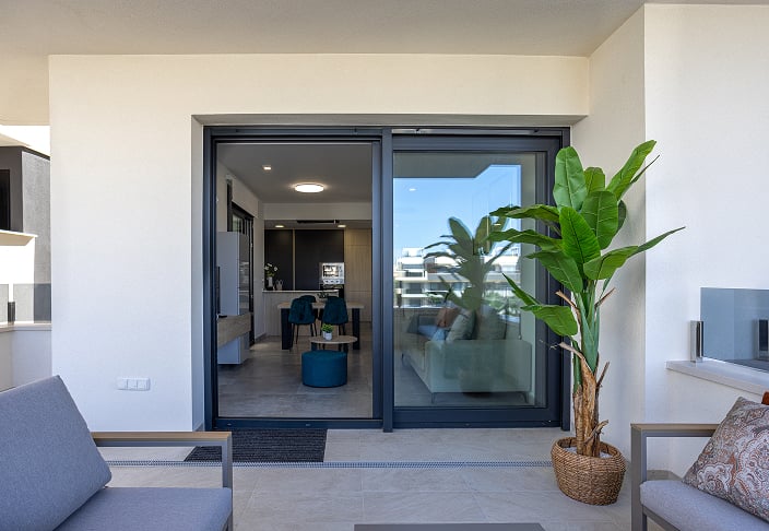 Dark-framed sliding patio door open from a furnished patio into a living room and kitchen