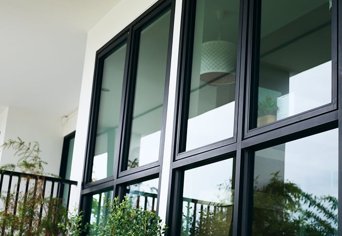 Tall black-framed awning windows along the white exterior wall of a home, with greenery in the foreground