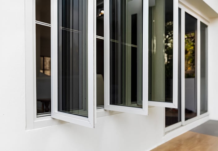 Three white casement windows cranked open outward from a white exterior wall