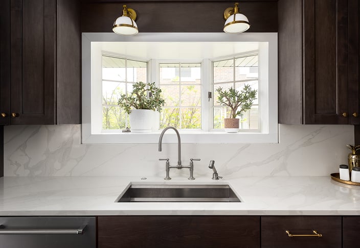 Garden window above a kitchen sink holding potted plants, set into a white surround between dark cabinets