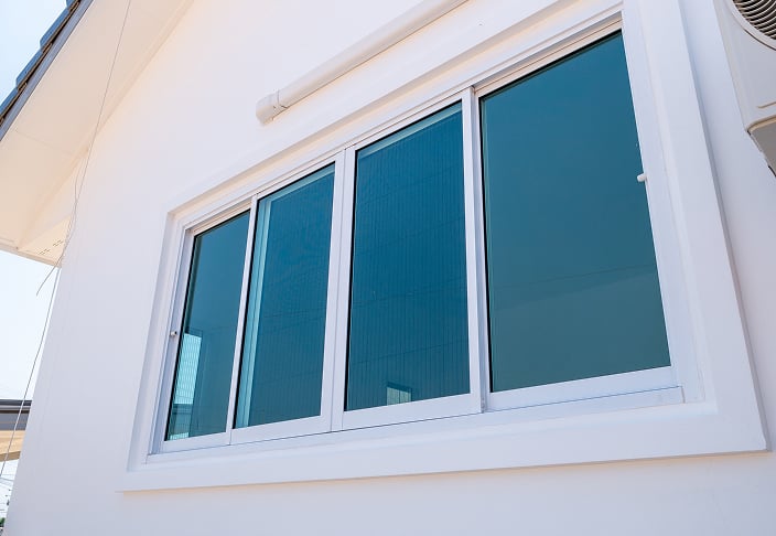 White-framed horizontal slider window with tinted glass on the exterior wall of a home